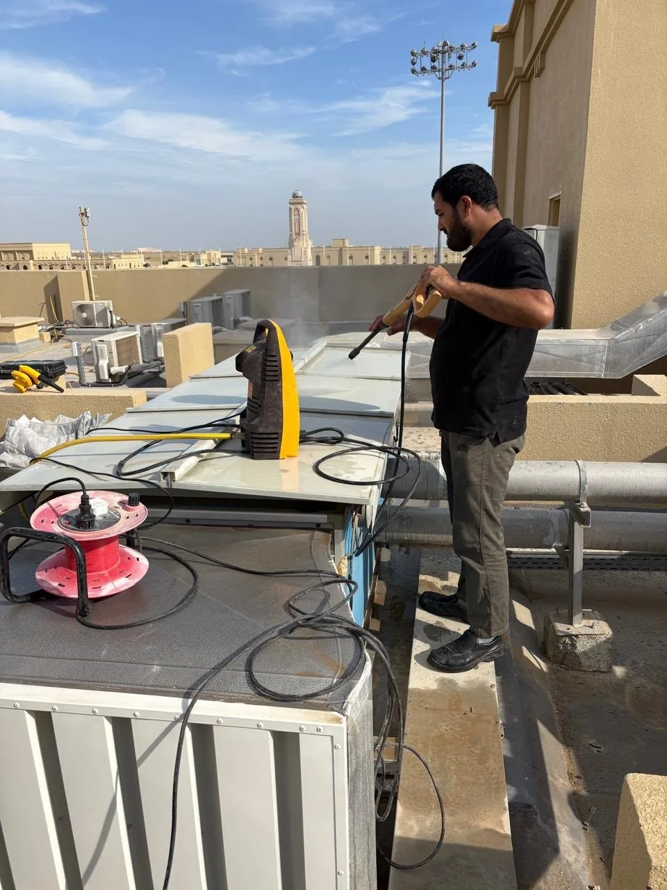 Technician cleaning a rooftop air-conditioning unit with a pressure washer